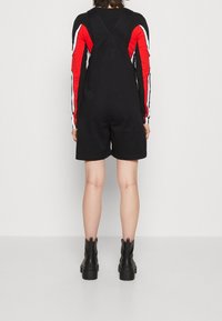 Svarta hängselshorts med justerbara remmar, stylade med en långärmad topp med röda och vita randiga ärmar, ihop med kraftiga svarta stövlar.