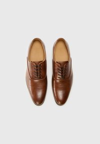Zapatos de cuero marrón con una textura suave, diseño de punta afilada y cordones negros. El interior tiene un forro de un marrón claro. Sin marcas visibles.