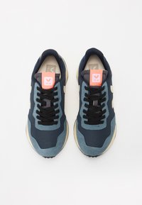 Marineblå og teal joggesko med teksturert stoff, hvite detaljer, svarte snøringer og en rosa logotab. Gummisåler med et sporty design.