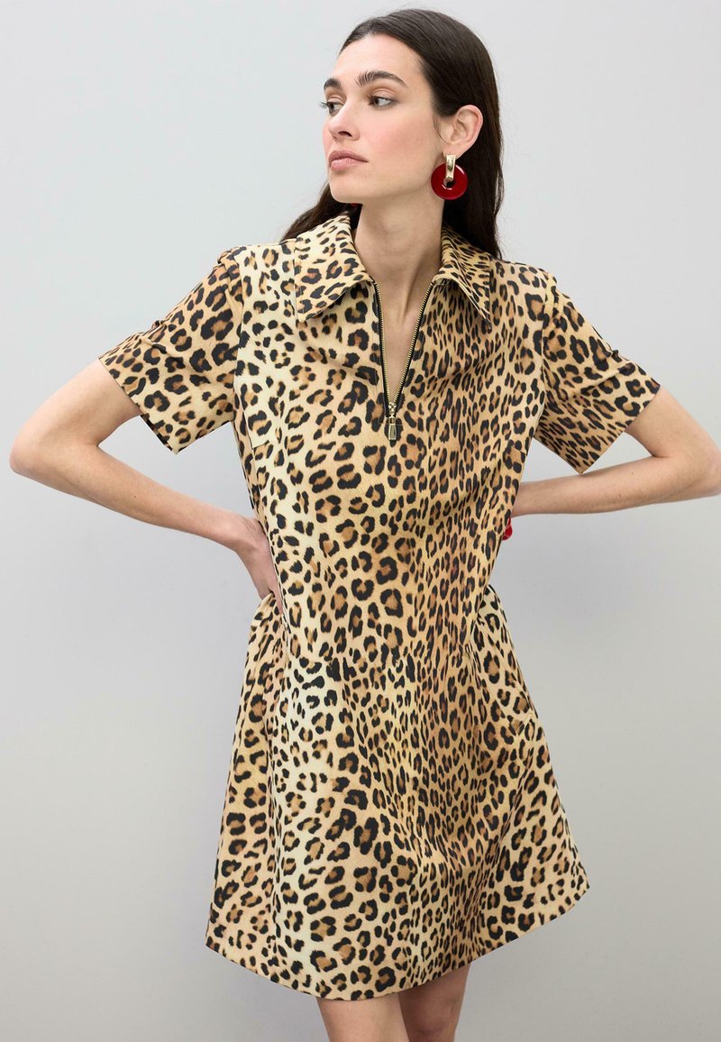 Robe imprimé léopard avec manches courtes, col zippé et forme trapèze. Le tissu a une texture douce avec des nuances variées de brun et des taches noires.