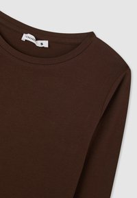 Maglia marrone a maniche lunghe realizzata in un tessuto morbido e liscio. Presenta un colletto curvo e un design semplice, l'etichetta indica la taglia small.