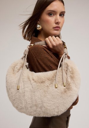 Sac à main en fausse fourrure crème avec une forme arrondie. Il dispose de anses en cuir beige avec des accents en métal doré, mettant en valeur un extérieur doux et texturé.