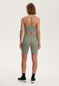 Grön aktivkläder-set i olivgrönt som består av en figurnära sport-bh med korsade axelband och högmidjade shorts. Slen textur, sportig design.