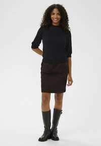 Dark navy short-sleeve pullover and brown suede skirt with two front pockets, paired with knee-high black leather boots.