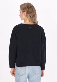Navyblauwe gebreide trui met een relaxte pasvorm, ronde halslijn en ribgebreide boorden. Heeft een klein logodetail aan de achterkant.