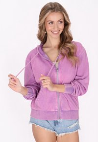 Felpa viola con zip e finitura testurizzata, dotata di cappuccio con cordino e polsini a coste, abbinata a pantaloni corti in denim.