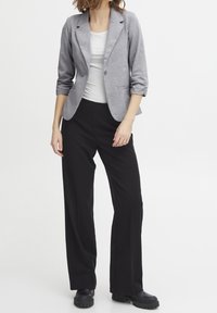 Grå stickad blazer med en enda knapp, med vikta ärmar. Matchad med svarta vida byxor och kraftiga svarta stövlar.