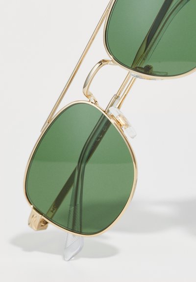 Ochelari de soare cu ramă aurie, dotati cu lentile mari verzi, având o formă rectangulară și tampoane nazale transparente. Temele subțiri îmbunătățesc designul elegant.