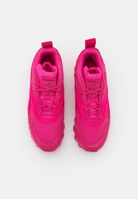 Rosa sneakers med ett texturerat tygöverdrag, släta detaljer och förstärkt häl. Har platta snören och en dragflik för enkel användning.