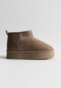 Hnědé semišové kotníkové boty s jednoduchým designem, kulatou špičkou a strukturovanou gumovou podrážkou s vlnkovým vzorem. Malá poutka na zadní straně.