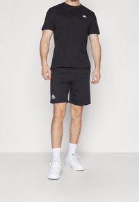 Černý set trička a šortek; měkký bavlněný materiál; logo na hrudi a šortkách; čistý design; v kombinaci s bílými teniskami a ponožkami.