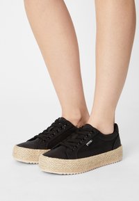 Černé plátěné tenisky s platformou z proplétané juty, kovovými průchody na tkaničky, černými tkaničkami a nenápadným logem na boku.