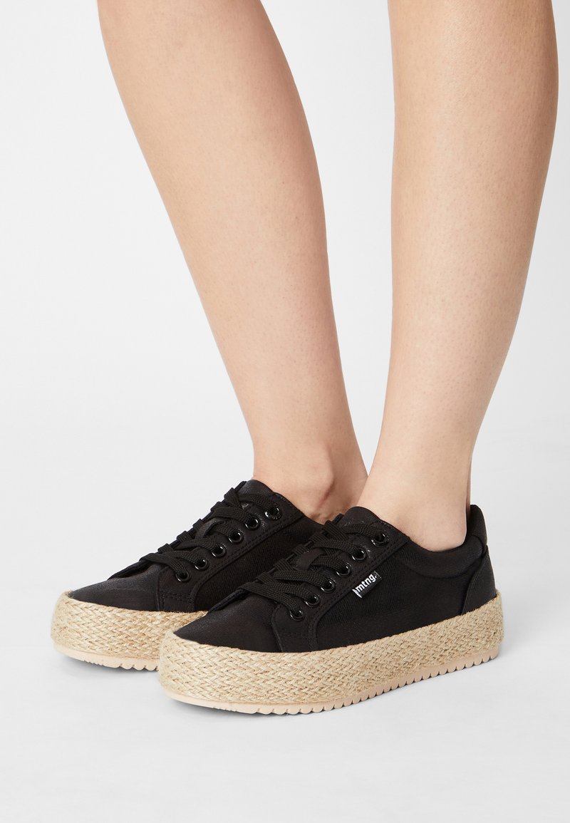 Černé plátěné tenisky s platformou z proplétané juty, kovovými průchody na tkaničky, černými tkaničkami a nenápadným logem na boku.