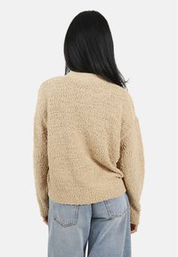 Pull en tricot texturé beige à coupe décontractée, encolure ronde et bord-côte. Associé à un jean en denim bleu clair taille haute.