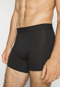 Schwarze Boxershorts mit elastischem Bund, Logo auf dem Bund gedruckt, taillierte Passform und glatte Baumwollstoffstruktur.