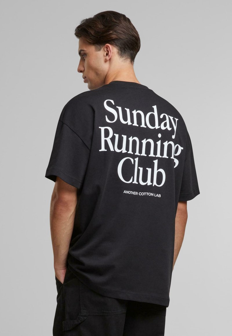 Black cotton t-shirt featuring large white text on the back reading "Sunday Running Club" and "ANOTHER COTTON LAB" underneath.