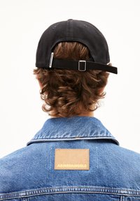 Schwarze Baumwollmütze mit verstellbarem Riemen und kleinem Logo-Tag. Jeansjacke mit einem beigen Etikett, das "ARMEDANGELS" auf dem Rücken zeigt.