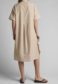 Beżowa lniana sukienka z kołnierzykiem, krótkimi rękawami, plisowanym tyłem i bocznymi rozcięciami. Gładka tekstura i luźny krój zapewniają wygodę noszenia.
