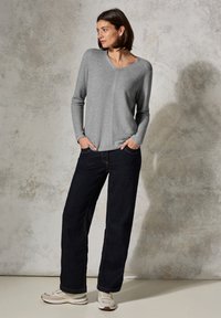 Grå, långärmad v-ringad tröja med en lätt strukturerad yta, kombinerad med vida, mörka jeans och ljusa sneakers.