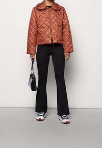 Pikowana brązowa kurtka z falbanianym kołnierzem, guzikami z przodu i dwoma bocznymi kieszeniami. Noszona z czarnymi rozszerzanymi spodniami i czarną torebką. Casualowe trampki.