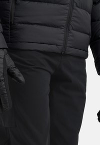 Zwarte gewatteerde jas met isolatie en een textuur, voorzien van een ritssluiting en aansluitende manchetten, gecombineerd met bijpassende zwarte broek en handschoenen.