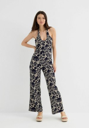 Mono impreso en azul marino y beige con cuello halter, piernas anchas y patrones abstractos de hojas. Fabricado con una tela ligera y texturizada.