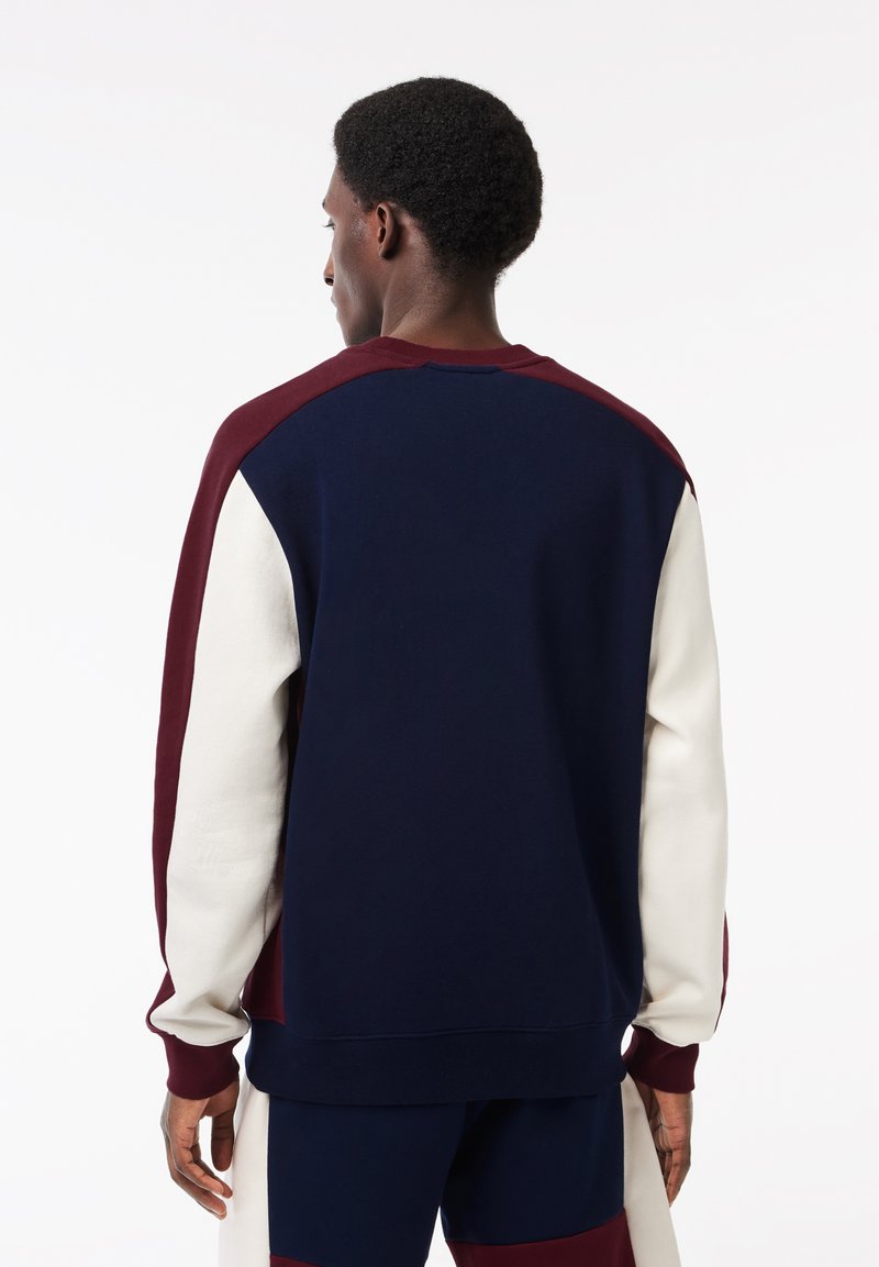 Sudadera de cuello redondo con bloque de color en azul marino, burdeos y crema. Está hecha de una tela suave, tiene puños acanalados y un corte relajado.