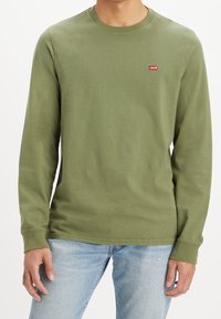 Långärmad grön skjorta i bomull med rund halsringning och en liten röd Levi's-logotyp på bröstet. Bärs med ljusa jeans.