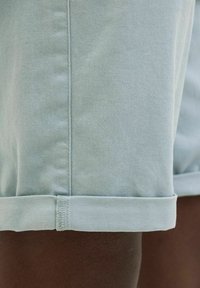 Ljust blå denimshorts med uppvikta muddar, har en slät yta, rak skärning och synlig sömnad längs sömmarna.