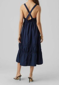 Marinblå bomullslenkjol med korsade axelband, rynkad midja och lager på lager-skirt. Slät textur med en flödande silhuett, knälång design.