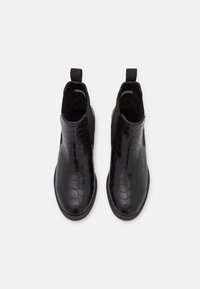 Musta nilkkureita, jotka on valmistettu kiiltävästä krokotiilikuosisesta materiaalista, joissa on joustavat sivupaneelit ja vetotapit helppoa pukemista varten. Pinnan sileä rakenne ja pyöreä kärki.