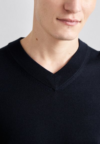 Mornarsko modra v-izrezana pulover iz mehke pletenine, z ribastim ovratnikom, slim fit krojem in gladko teksturo. Poudarjen posnetek zgornjega dela telesa.