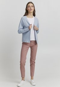 Svijetloplava kardigan s opuštenim krojem i otvorenim prednjim dijelom, uparen s bijelom majicom, ružičastim hlačama i bijelim tenisicama. Minimalistički dizajn.