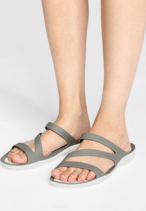 Infradito grigie con due cinturini incrociati, realizzate in materiale liscio, dotate di una suola bianca e design con punta aperta. Flessibili e leggere.