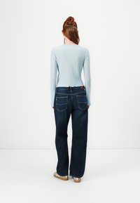Light blue ribbed long-sleeve top paired with high-waisted dark blue wide-leg jeans. Notable back pocket stitching and casual fit.