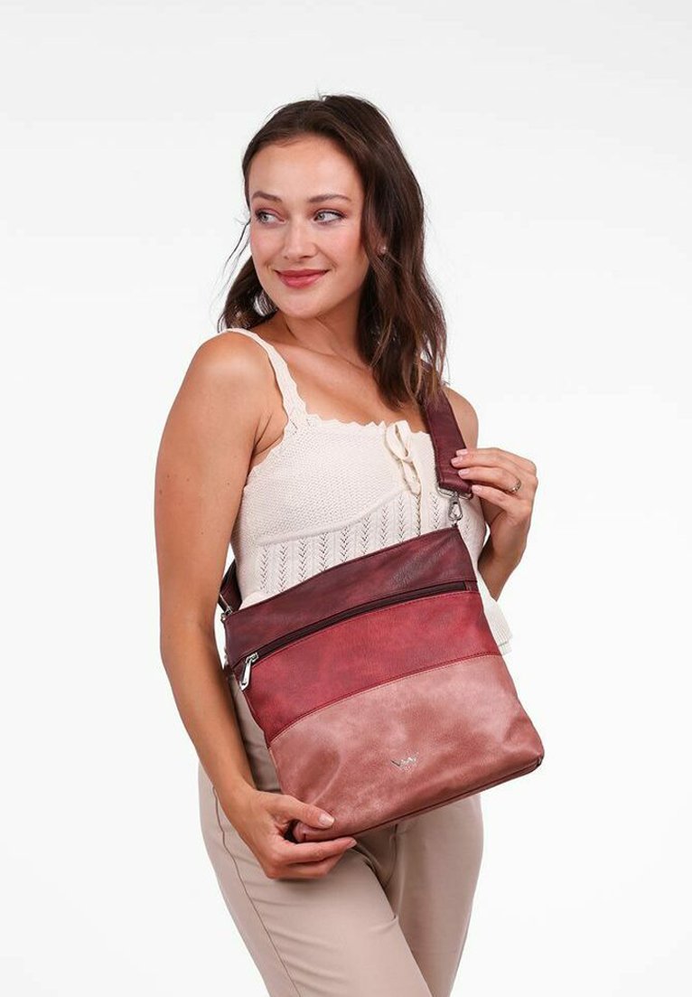 Červená ombre crossbody taška se zipem, která má dvě texturované panely—hladký tmavě červený a světle růžový—nastavitelný popruh a akcent s logem.