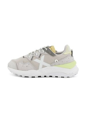 Scarpa sportiva grigia e bianca realizzata in materiali mesh e suede, con un accento verde sul tallone e una suola bianca a fantasia. Presenta lacci riflettenti.