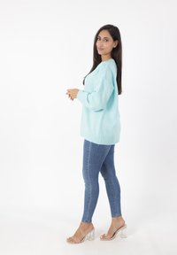 Maglione azzurro chiaro a maglia con spalle scese, maniche lunghe e orlo a costine, abbinato a jeans skinny blu scuro e sandali con tacco a blocco trasparente.