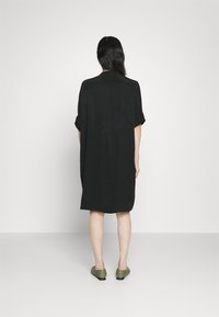 Czarna dzianinowa sukienka z krótkim rękawem, luźny krój, z teksturowanym wzorem. Połączona z zielonymi balerinami, widok z tyłu na jednolitym tle.