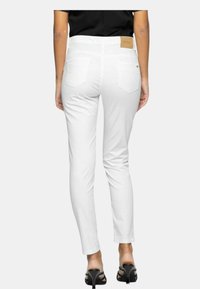 Jeans skinny bianchi con una texture liscia, design a cinque tasche e una patch con marchio nella parte posteriore della vita, abbinati a sandali neri con tacco.