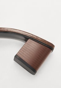Sandale à talon marron avec une tige en cuir lisse, un talon carré à finition texturée et une semelle en caoutchouc noir pour plus d'adhérence.