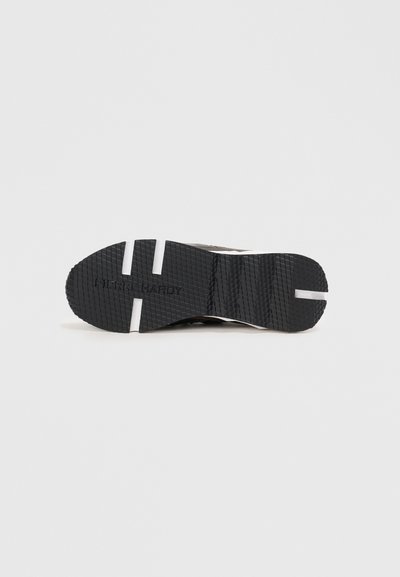 Suela de zapatilla negra con patrón de agarre texturizado, nombre de la marca en relieve y rayas de acento blancas. La forma plana mejora la estabilidad y la tracción.