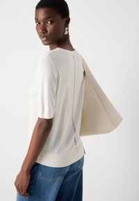 Pull à manches courtes, couleur crème, fabriqué en tissu doux. Il présente un ourlet côtelé, un détail de couture au dos, et est associé à un sac beige et à un denim.