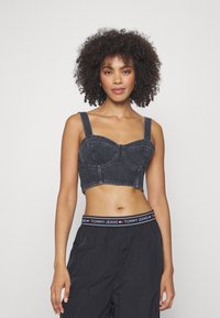 Sötét mosású farmer cropped top, struktúrált mellekkel, széles pántokkal és testhez simuló fazonnal. Fekete nadrággal viselve, látható logózott derékrésszel.