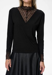 Czarna bluzka z długim rękawem i koronkowym, wysokim dekoltem, ozdobiona misternymi wzorami oraz koronkowymi mankietami. Gładki materiał z dopasowanym krojem.