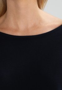 Marinblå, lätt stickad topp med bred båturringning och slät textur; tyget verkar mjukt och stretchigt, lämpligt för avslappnad användning.