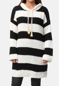 Vestito con cappuccio in maglia a righe bianche e nere, con cappuccio regolabile a coulisse, dettagli con nappine e maniche lunghe, presentato su uno sfondo neutro.