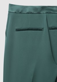 Pantaloni di stoffa verdi con una texture liscia, caratterizzati da una vita in satin e due tasche posteriori con rifiniture in velluto.
