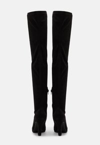 Botas de ante negras por encima de la rodilla con un diseño ajustado, puntera en punta y tacones medios; cuentan con cremalleras en los lados interiores.