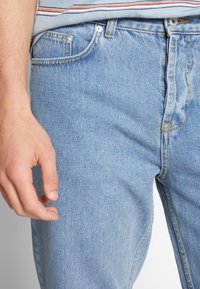 Jasnoniebieskie dżinsy z denimu o klasycznym kroju prostych nogawek, z delikatną fakturą, pięciokieszeniowym wzorem oraz detalami kontrastującego przeszycia.